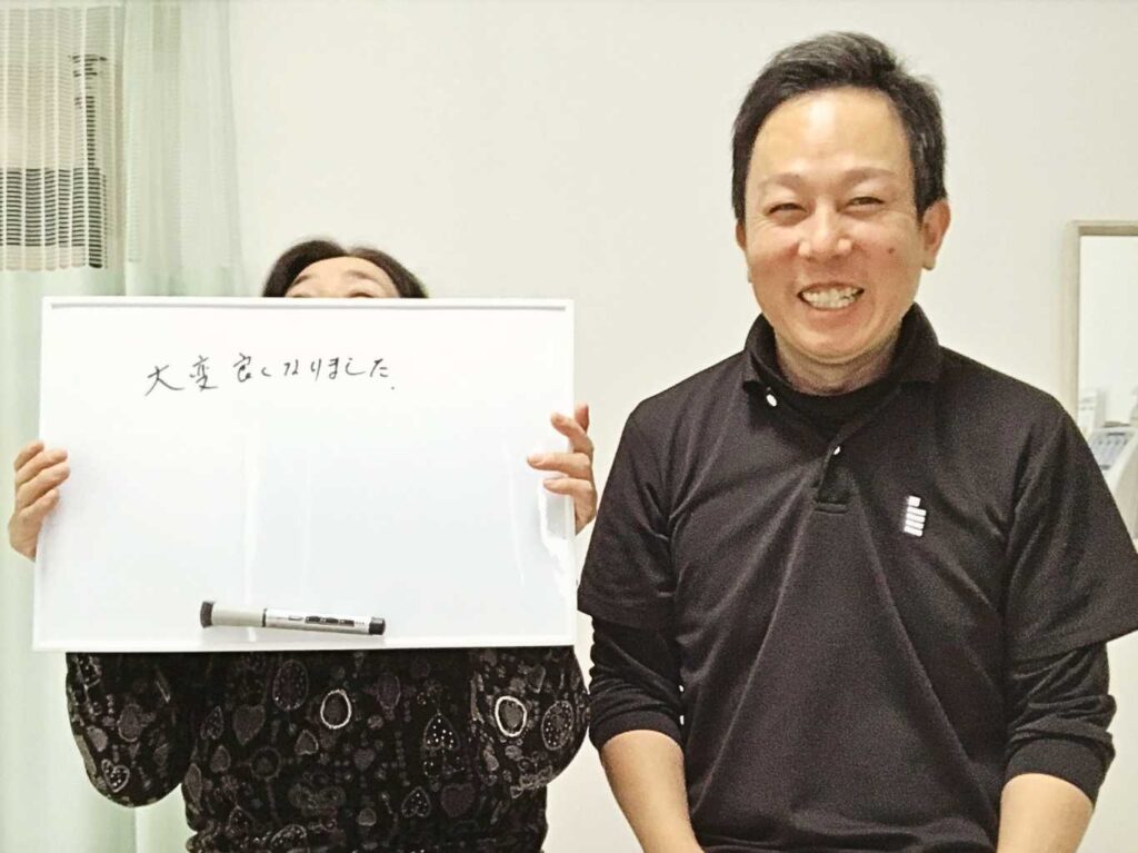 「大変良くなりました」と書かれたホワイトボードを持つ60代女性の患者様と、笑顔のはる整体院の院長