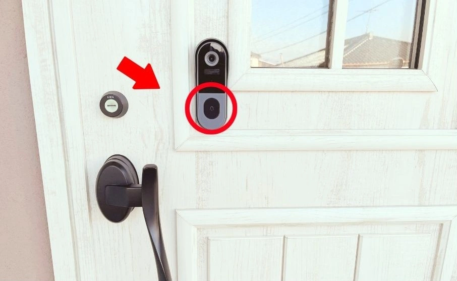 玄関ドアに取り付けられたカメラ付きインターホン。押しボタンの位置を赤い矢印と赤丸で示しています